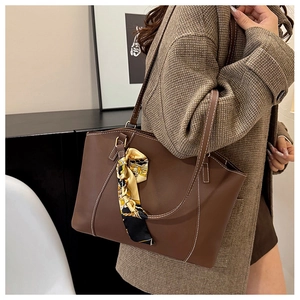 Detail of brown leather tote bag with white contrast stitching and a silk scarf accent