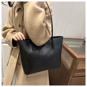 Detail of black faux leather tote bag with vertical stitching shown on shoulder