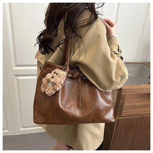 Brown leather tote bag featuring a leather strap detail and a cute plush dog charm
