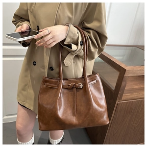 Close-up of brown vintage leather tote bag with metal buckle detail and shoulder strap
