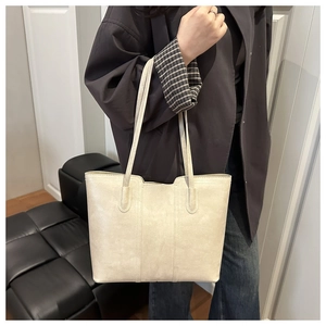 Close-up of a large beige tote bag with vertical stitching and slim shoulder straps