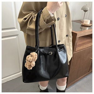 Close-up of black leather tote bag with elegant buckle detail and plush teddy bear charm