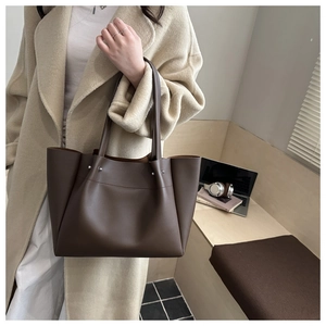 Detail view of large dark brown leather tote bag carried with beige wool coat