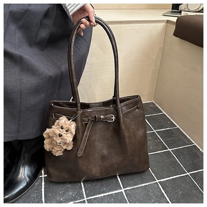 Detail of dark brown tote bag featuring belt buckle decor and plush puppy charm