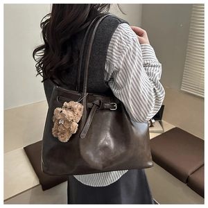 Detail of dark brown leather tote bag with plush bear charm and tie decoration