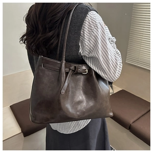 Detail of a dark brown leather tote bag with belt buckle and slim straps on a model