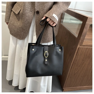 Dettaglio della borsa tote nera in pelle con fibbia dorata portata da modella in blazer