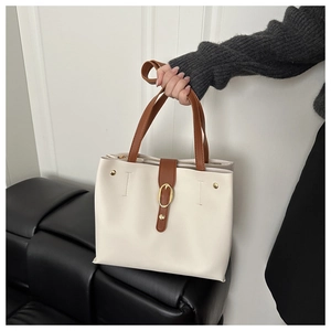 Détail d'un sac cabas beige avec anses brunes, garniture dorée et boucle décorative