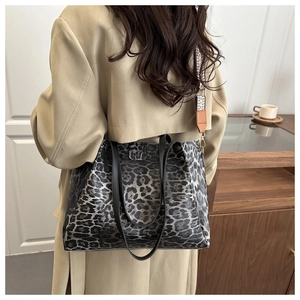 Detail of leopard print tote bag with black leather handles and woven shoulder strap