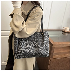 Detail showing the leopard print pattern, golden rivets, and black leather strap of the tote bag