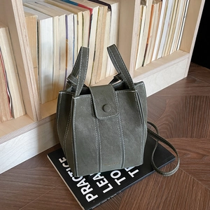Minimalist dark green bucket bag with white contrast stitching on a wooden surface