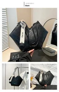 Dettaglio della borsa tote nera intrecciata con ampia tracolla in tessuto e targhetta in metallo