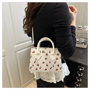 Vue portée montrant la taille du sac à bandoulière en cuir blanc à motif cerises