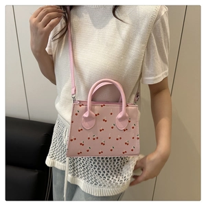 Détail d'un mini sac rose avec imprimé cerise porté par un mannequin dans une pièce