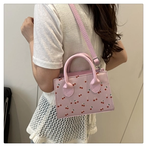 Pink cherry print tote bag with adjustable shoulder strap worn by model in casual style