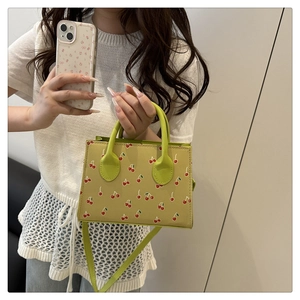 Detail of crossbody bag featuring red cherry prints and contrasting green top handle