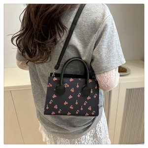Detail view of mini black crossbody bag with cherry print on a model in a minimal interior