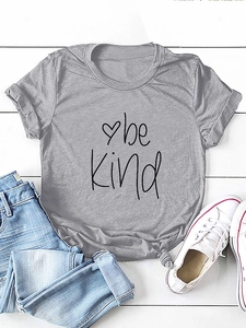 Detail of grey Be Kind cotton t-shirt with heart graphic styled on white wood background