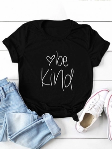 Detail of Be Kind black t-shirt with knotted hem and heart print on a wooden background