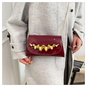 Detail showing high-gloss wine red leather texture and wavy gold metal buckle on evening bag