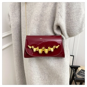 Detail of burgundy patent leather bag with wave gold buckle worn over a grey coat
