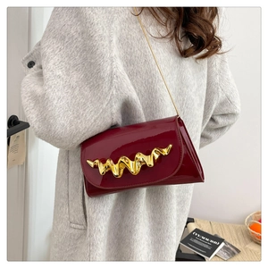 Detail of burgundy glossy handbag with a gold wave-pattern buckle on grey coat
