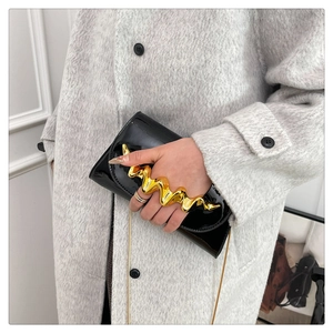 Detail of glossy black patent evening clutch featuring unique gold wavy metal handle