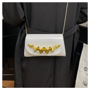 Detail of white glossy leather bag with decorative gold wave metal hardware and chain