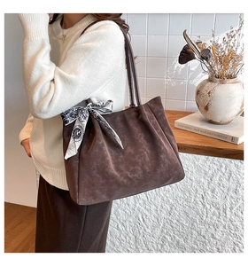 Detail of brown suede tote bag with pleated design and silk scarf on handle