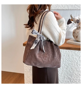 Detail of a brown soft leather tote bag featuring a decorative printed silk scarf on handle