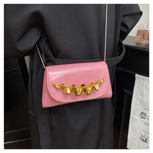Detail of hot pink patent leather clutch with gold wave accent and slim chain strap