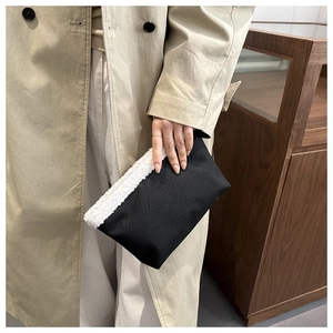 Dettaglio pochette nera in fibra sintetica con bordo in shearling bianco e cerniera