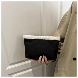 Dettaglio di una borsa a mano nera con bordo in peluche bianco tenuta da un modello
