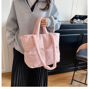 Detail of pink quilted puffer tote bag held by a model in a casual hoodie outfit