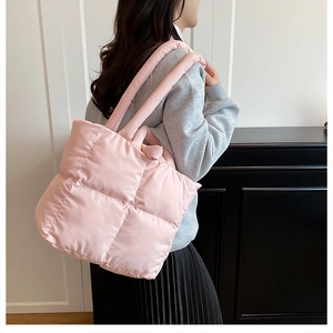 Close-up of pink quilted puffer tote bag worn by a model in a modern interior setting