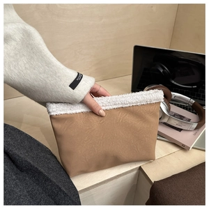 Dettaglio di una pochette in pelle scamosciata marrone con bordo in peluche bianco