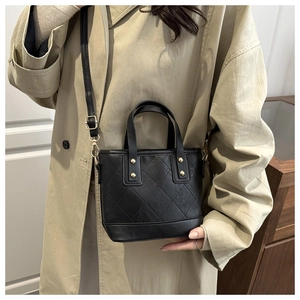 Détail du sac seau noir matelassé avec garnitures dorées et bandoulière sur un manteau beige