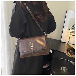 Donkerbruine retro crossbodytas met gouden gesp gestyled op een zwarte trenchcoat