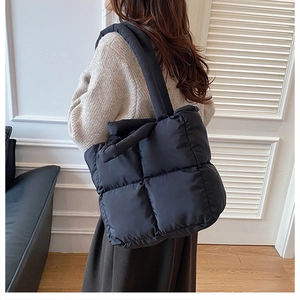 Close-up of black quilted puffer tote bag shoulder strap and soft nylon padded texture