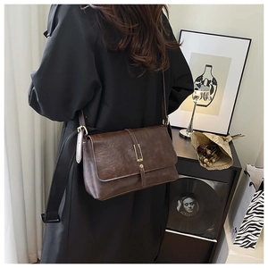 Detailweergave van een vintage donkerbruine lederen crossbodytas op een zwarte trenchcoat