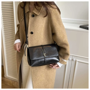 Detail van vintage zwarte leren crossbodytas met metalen slot op bruine wollen jas