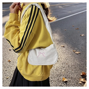 Dettaglio borsa sottobraccio in velluto bianco con fiocco rosa ricamato su felpa gialla