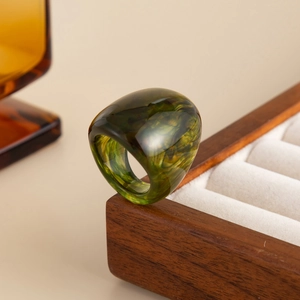 Macro shot of chunky green amber resin dome ring with vintage marble texture on wood box