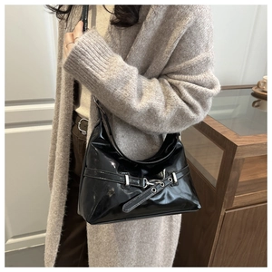 Detail of a black shiny hobo underarm bag with silver buckles shown on a model