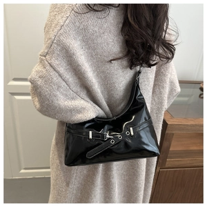 Black patent leather crescent shoulder bag shown on model with belt buckle detail