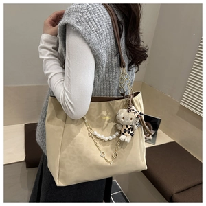 Dettaglio della borsa tote crema con catena di perle, accenti dorati e ciondolo leopardo