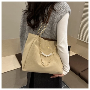 Modella con borsa tote beige con tracolla a catena e ciondolo di perle in interni