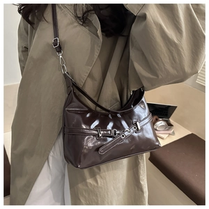 Deep brown glossy patent leather shoulder bag with buckle strap detail on a model