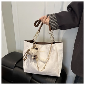 Dettaglio della borsa tote bianca con catena dorata, manico in pelle e charm leopardato