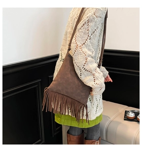 Close-up of a dark brown suede shoulder bag with long bohemian tassels on a model
